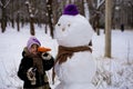 A small cheerful girl holds a big carrot, the nose of a big snowman Royalty Free Stock Photo