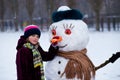 A small cheerful girl holds a big carrot, the nose of a big snowman Royalty Free Stock Photo