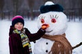 A small cheerful girl holds a big carrot, the nose of a big snowman Royalty Free Stock Photo