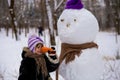 A small cheerful girl holds a big carrot, the nose of a big snowman Royalty Free Stock Photo