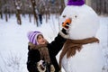 A small cheerful girl holds a big carrot, the nose of a big snowman Royalty Free Stock Photo