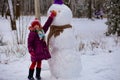 A small cheerful girl holds a big carrot, the nose of a big snowman Royalty Free Stock Photo