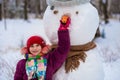 A small cheerful girl holds a big carrot, the nose of a big snowman Royalty Free Stock Photo