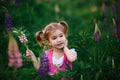 A small cheerful girl with two light tails on her head in a green field with purple flowers.