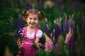 A small cheerful girl with two light tails on her head in a green field with purple flowers.