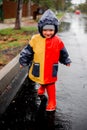 A small child, alone in the rain, runs on kalyuzh. In a raincoat in blue, red and orange colors and red boots.  Happy child. Caref Royalty Free Stock Photo