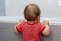 A small child in the bathroom looking into the bath, holding the edge Royalty Free Stock Photo