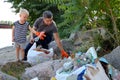 A small child collects trash on the beach. His dad points his finger where to throw garbage. Parents teach children cleanliness.