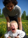 A small child cries very much. Mom tries to hold him with her hands and stop the tantrum. The kid is not happy. He is wearing a Royalty Free Stock Photo