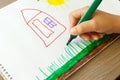A small child draws a house with markers in the album. Step-by-step instructions