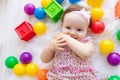 A small child girl lies in red clothes on a white Mat among toys balls and cubes and sucks her finger Royalty Free Stock Photo