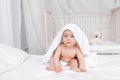 A small child a girl 6 months old lies in a towel on a white bed in a bright nursery in diapers after bathing Royalty Free Stock Photo