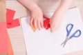 A small child glues paper, children`s safe scissors and colored paper on the table