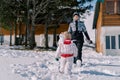 Small child goes to his mother standing next to a snowman in the yard. Back view Royalty Free Stock Photo