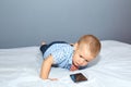 A small child lies on a bedspread and looks at a mobile phone Royalty Free Stock Photo