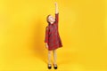 A small child measures her growth on a yellow background. Full-length girl in a red dress. Development concept, goal, success Royalty Free Stock Photo