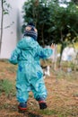 Small child in overalls walks through the dry grass in the garden. Back view