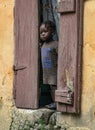 Small child looks out the wooden door of her concrete house in Haiti.