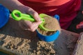 A small child puts a toy in a blue mug green sand shovel.