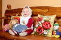 A small child in a shawl sitting on a sofa with embroidered pillows Royalty Free Stock Photo