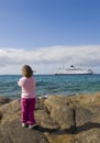 A small child on the shore watching a ship at sea