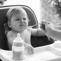 small child sits on a chair and eating with spoon. little smiling girl sits in baby-chair and have a breakfast