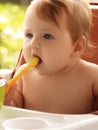 small child sits on a chair and eating with spoon. little smiling girl sits in baby-chair and have a breakfast