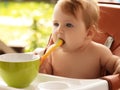 small child sits on a chair and eating with spoon. little smiling girl sits in baby-chair and have a breakfast