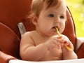 small child sits on a chair and eating with spoon. little smiling girl sits in baby-chair and have a breakfast