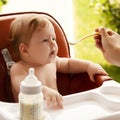 small child sits on a chair and eating with spoon. little smiling girl sits in baby-chair and have a breakfast