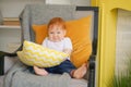 Small child sits in a chair and holds a pillow in his hands.