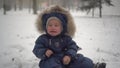 A small child sits in the snow in the park and cries from the cold. The boy in the down overalls had cold hands. Royalty Free Stock Photo