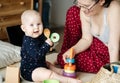 Small child is sitting on the floor holding a wooden spoon in his hands and happily playing with his mother in the interior of the