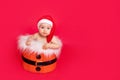 A small child of six months in a Santa hat sits in a basket on a red isolated photophone, a place for text, the concept of the new