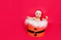 A small child of six months in a Santa hat sits in a basket on a red isolated photophone, a place for text, the concept of the new