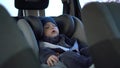 A small child sleeps in a car seat in a parking lot. Boy in a sweatshirt and hat. Royalty Free Stock Photo