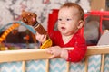 A small child stands and holds the edge of the bed or playpen in the nursery and playing with toy, happy and happy smiling baby, t Royalty Free Stock Photo