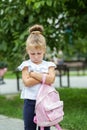 A small child stands offended on the street with a backpack. The concept of school, study, education, childhood