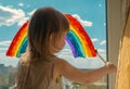 A small child stands on the windowsill and draws a rainbow on the window glass. multi-colored rainbow. symbol of happiness. select Royalty Free Stock Photo