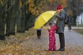 Small child stands in the yellow rain next to his mother in the park against the background of autumn yellow foliage