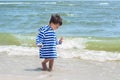 A small child in a striped robe is standing on the seashore in the water and looks at his wet legs to know the world, Royalty Free Stock Photo