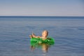 A small child swims across the sea in an inflatable circle and looks up.