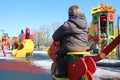 a small child on a swing in a park with children on rides playing on a walk