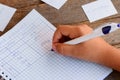 A small child is writing subject pronouns in the notebook. A notebook, a pen, paper cards with English words on a wooden table