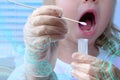 Small child, a 2-year-old blonde girl with open mouth, doctor takes cotton bud to analyze saliva, mucous membrane for DNA tests,