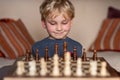 Small child 5 years old playing a game of chess on large chess board. Chess board on table in front of the boy thinking of next Royalty Free Stock Photo