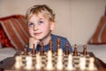 Small child 5 years old playing a game of chess on large chess board. Chess board on table in front of the boy thinking of next