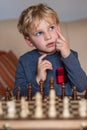 Small child 5 years old playing a game of chess on large chess board. Chess board on table in front of the boy thinking of next Royalty Free Stock Photo