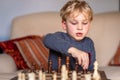 Small child 5 years old playing a game of chess on large chess board. Chess board on table in front of the boy thinking of next