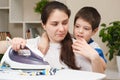 A small child of 4 years prevents his mother from ironing clothes. The difficulties of motherhood.